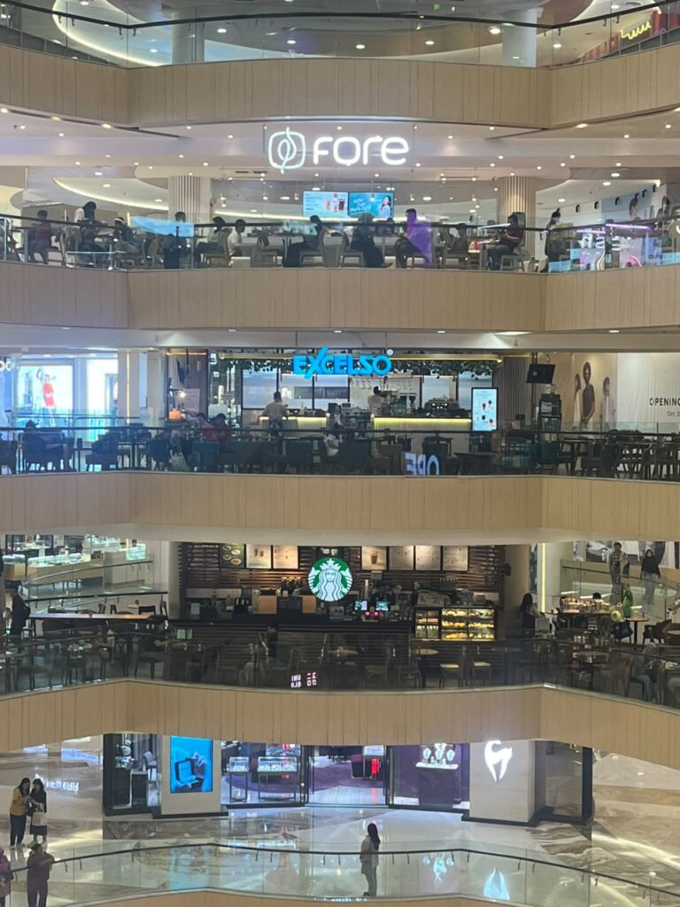 Tiga jaringan kedai kopi – Fore Coffee, Excelso, dan Starbucks – tampak berdiri secara vertikal di atrium Tunjungan Plaza, Surabaya, pada Minggu (26/7/2026)